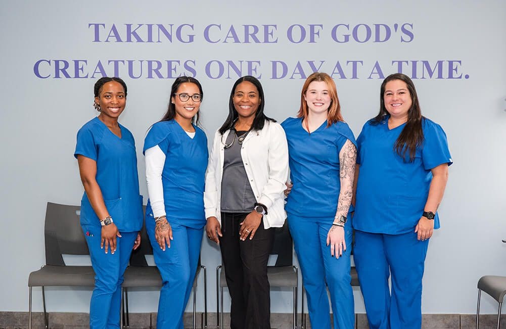 5 Members Of Van Crest Animal Hospital posing for camera in front of slogan wall