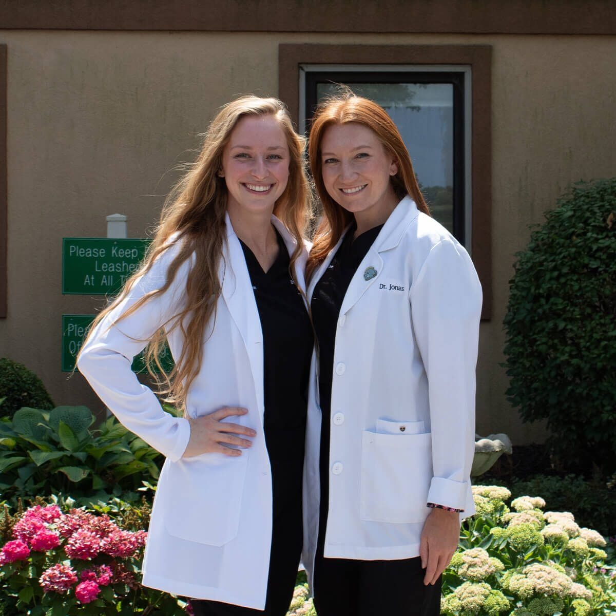 two young female veterinarians in lab coats smiling outside of vet hospital